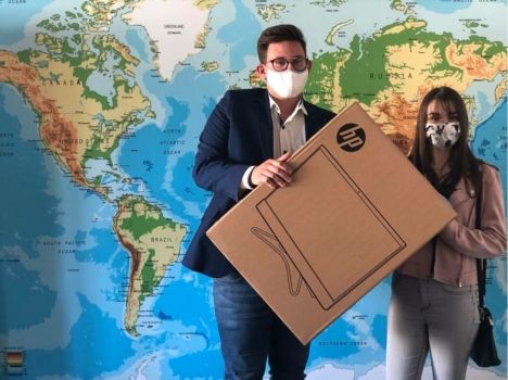 Na tel mapy świata, dwoje uczniów w maseczkach trzyma pudełko z nowym kompterem