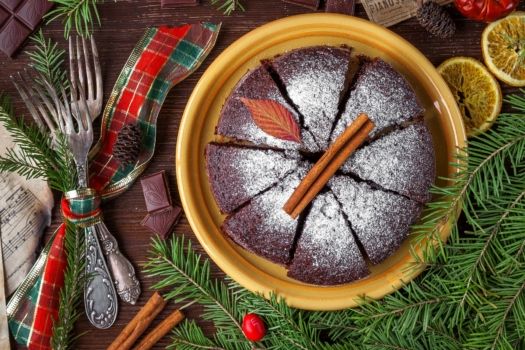 Ciasto świąteczne na żółtym talerzu, obok dekoracja świąteczna z gałązek choinki, cynamonu i suszonych pomarańczy