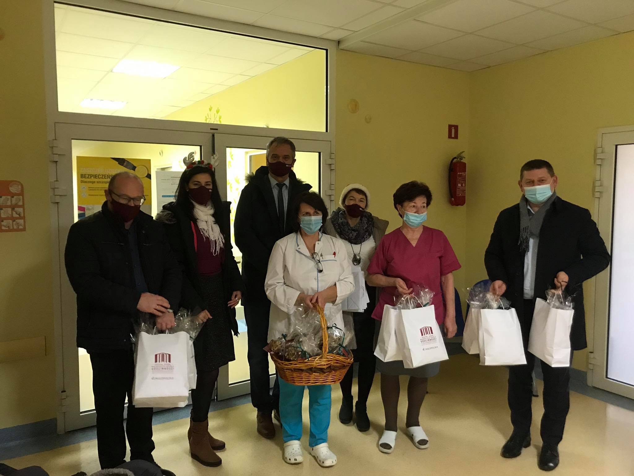 Grupa ludzi w szpitalnym korytarzu trzymająca białe pakunki z piernikami