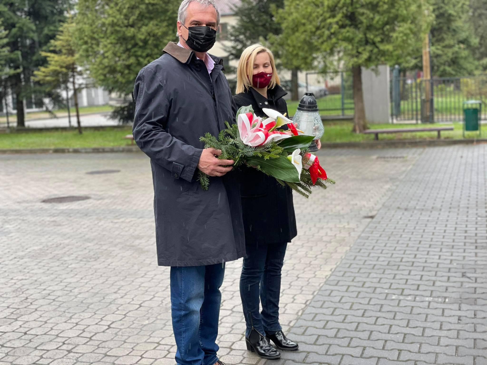 kobieta i mężczyzna z kwiatami i zniczem przed pomnikiem ofiar Katynia