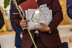na zdjęciu mężczyzna w bordowym garniturze, trzyma statuetkę i dyplom Nauczyciela Roku