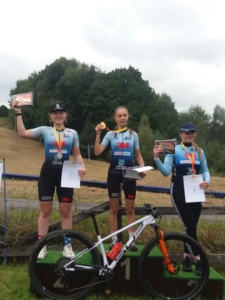3 dziewczyny stoją na podium w zawodach kolarskich