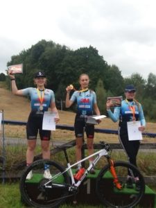 3 dziewczyny stoją na podium w zawodach kolarskich