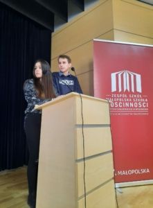 Dziewczyna i chłopak stoją przy mównicy i prowadzą debatę.