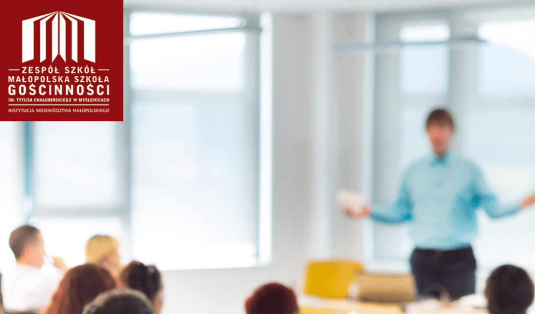 Rozmyte zdjęcie przedstawiające zebranie w sali, kilka osób siedzi na krzesłach i słucha stojącego z przodu mężczyzny, który prowadzi spotkanie. W lewym górnym rogu znajduje się logo szkoły, a na dole czerwony pasek z napisem: Zebranie z rodzicami uczniów klas LO i Technikum.